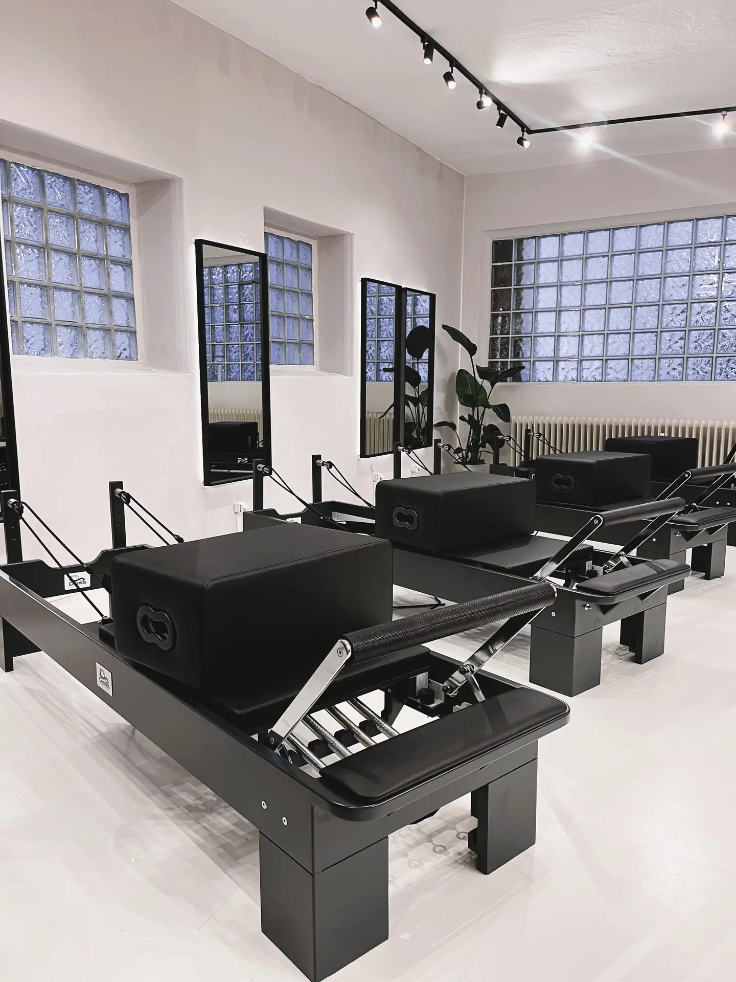 Helles Pilates Studio mit schwarzen Reformern und Spiegeln an Glasbausteinwaenden