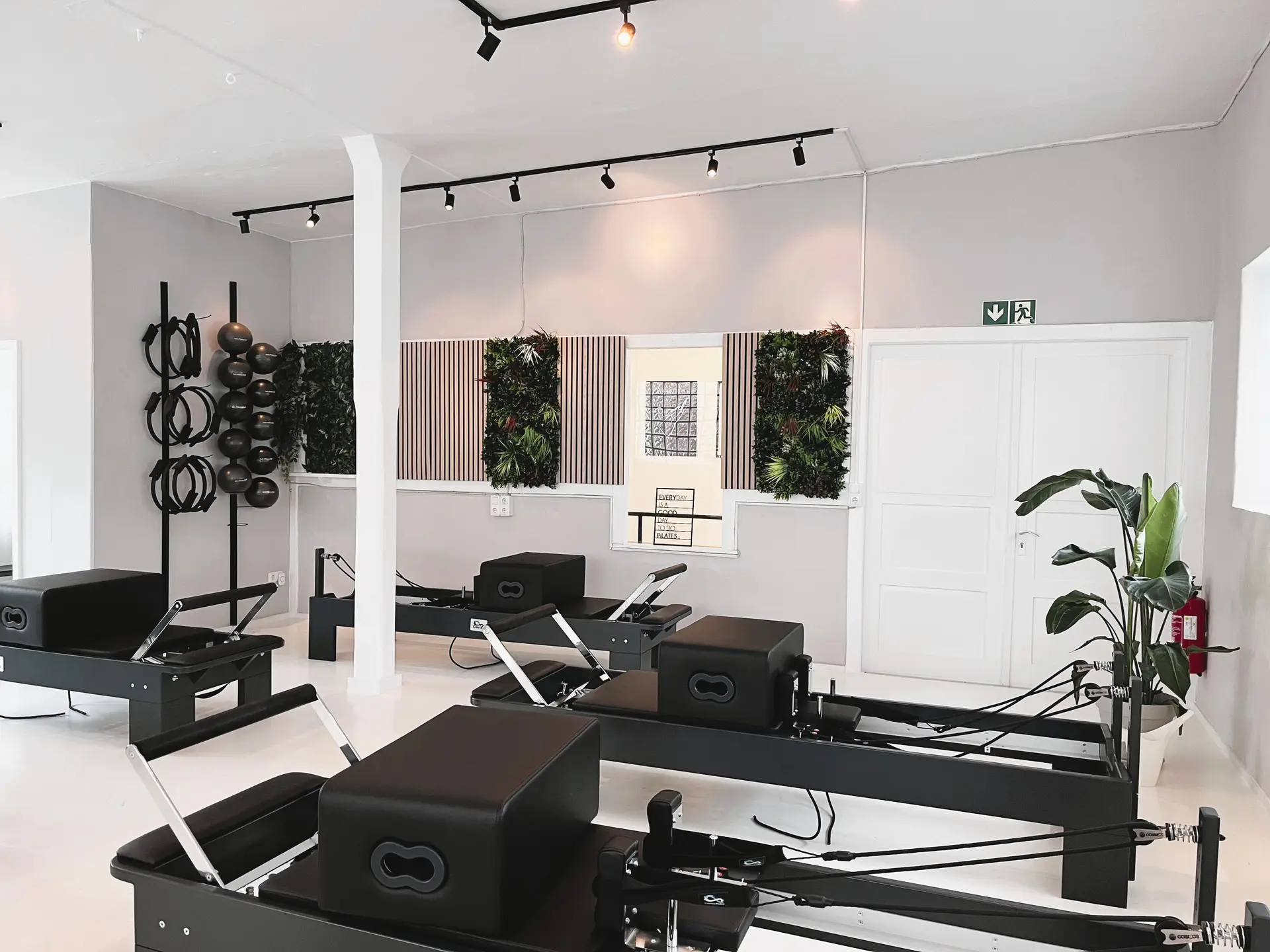 Helles Pilatesstudio ohne Personen mit schwarzen Geraeten und Pflanzenwanden